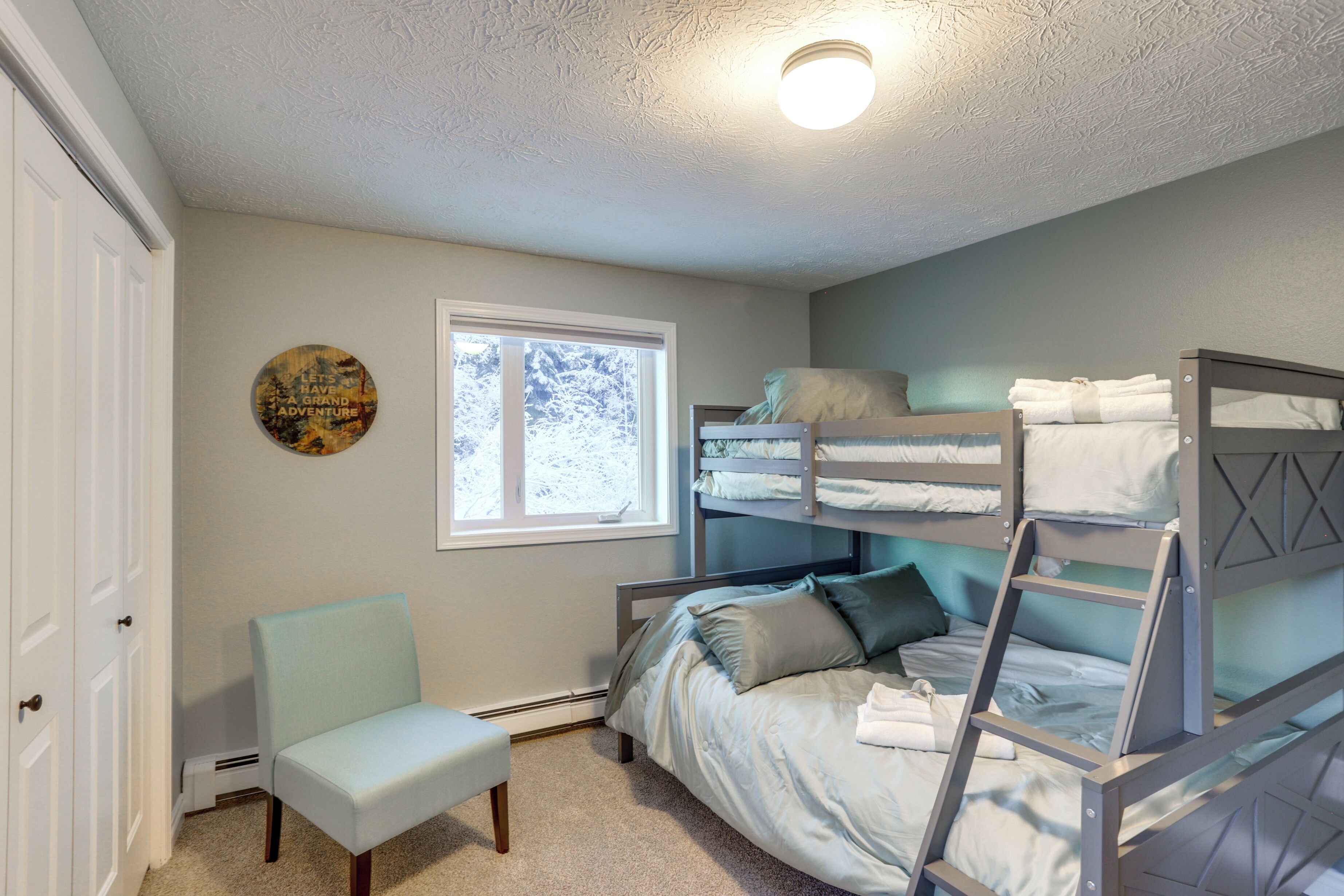 A bedroom with bunk beds, a chair, a window, and a door.
