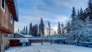 Une construction en bois avec un garage, une cour clôturée et des arbres couverts de neige.