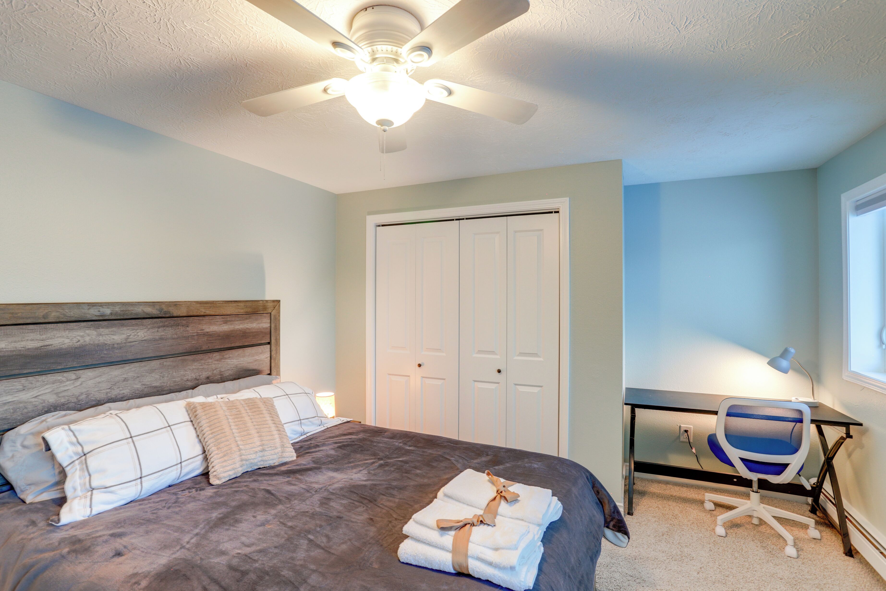 A bedroom with a bed, a desk, a chair, a ceiling fan, and a closet.