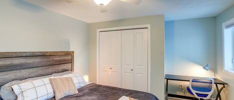 A bedroom with a bed, a desk, a chair, a ceiling fan, and a closet.