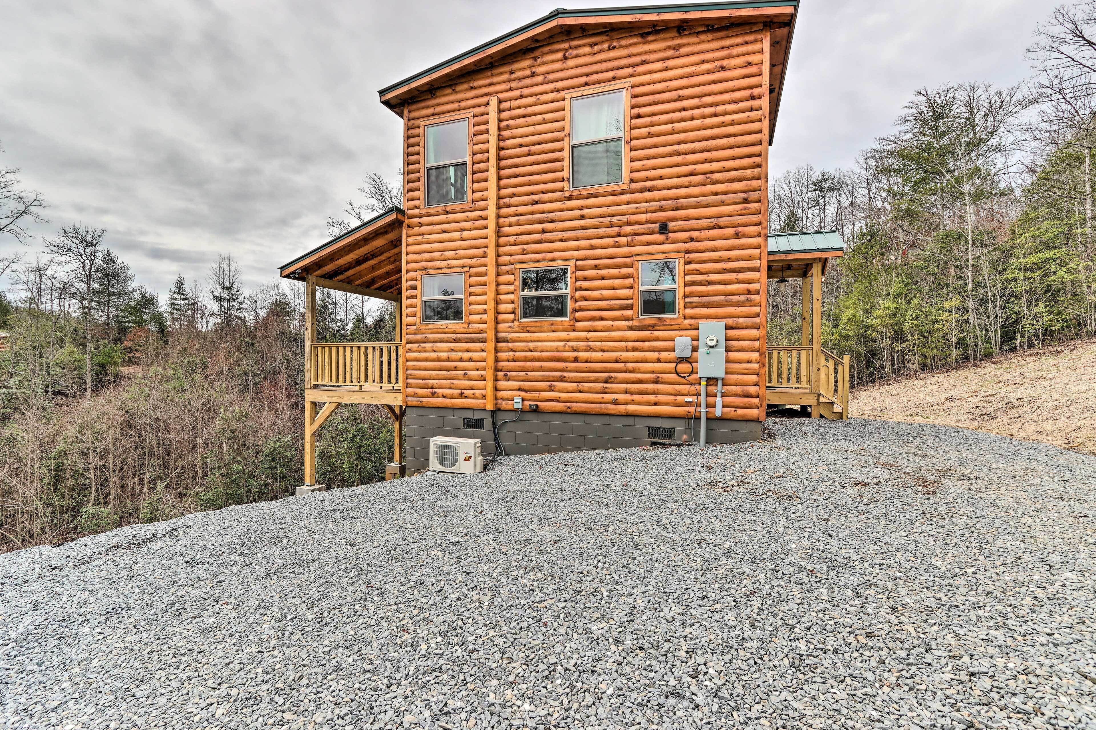A two-story log cabin with a porch and a gravel driveway.
