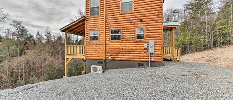 A two-story log cabin with a porch and a gravel driveway.