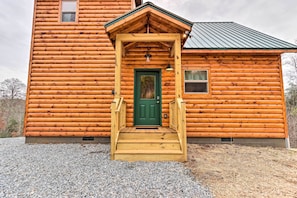 Une cabane en rondins avec une porte verte, des marches en bois et un petit porche.