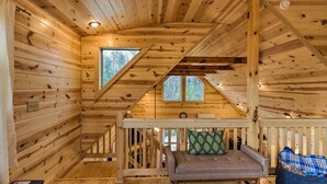 A cozy cabin interior with wooden walls, a loft bed, a sofa, and a window. - Cozy Mtn Cabin: Spacious Deck & Forest Views! (Murphy)