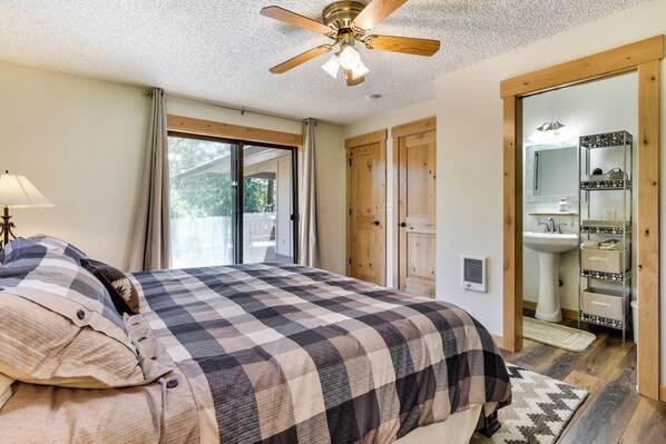 A bedroom with a large bed, a ceiling fan, a sliding glass door leading to a balcony, and a bathroom with a sink and mirror. - Riverfront Woodland Cabin: Wooded & Forested Views (Woodland)