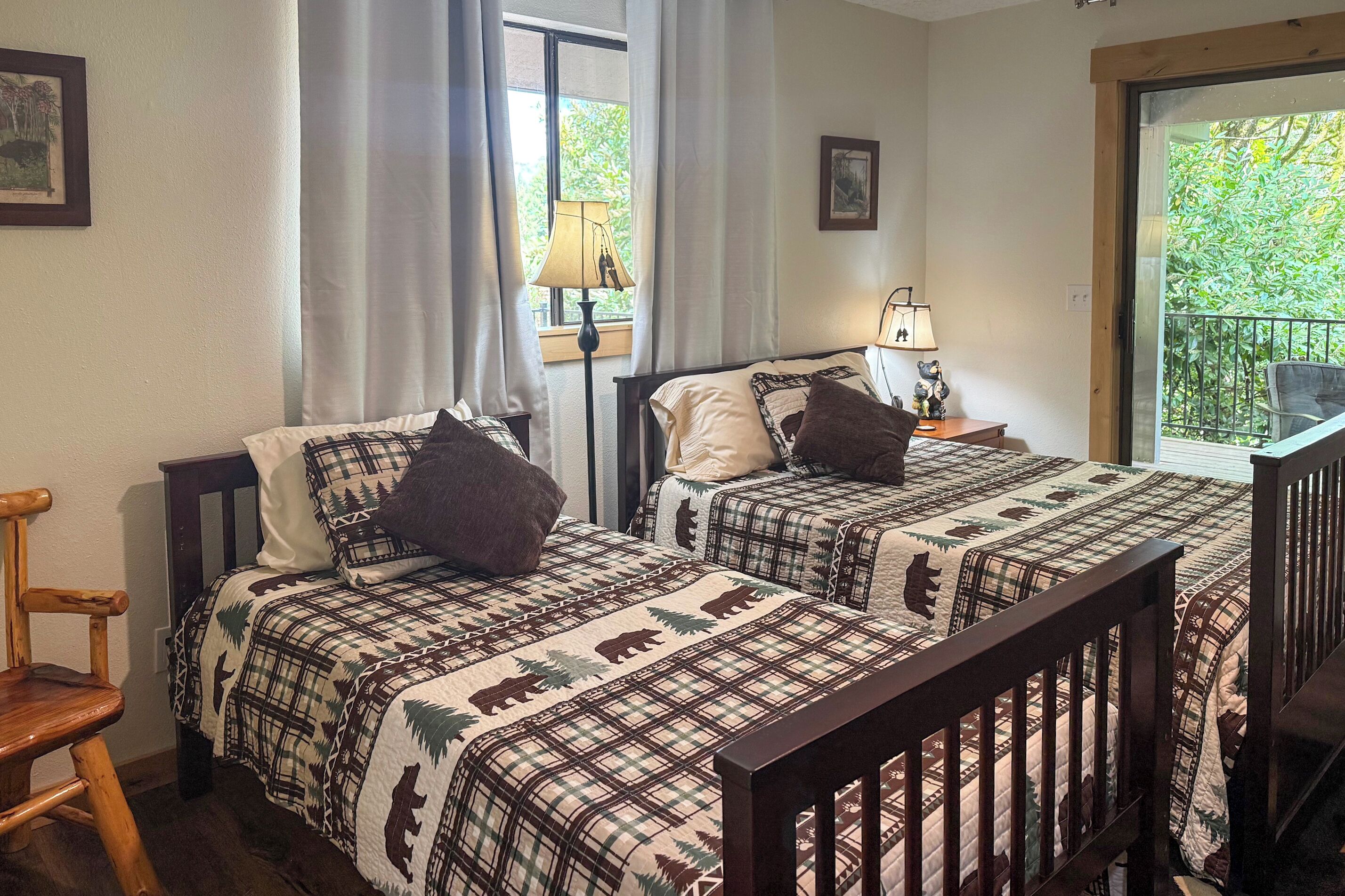 A room with two beds, a wooden chair, a window with curtains, and a balcony view.
