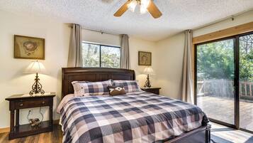 A bedroom with a large bed, two bedside tables with lamps, a ceiling fan, and a view of the outdoors through a sliding glass door.