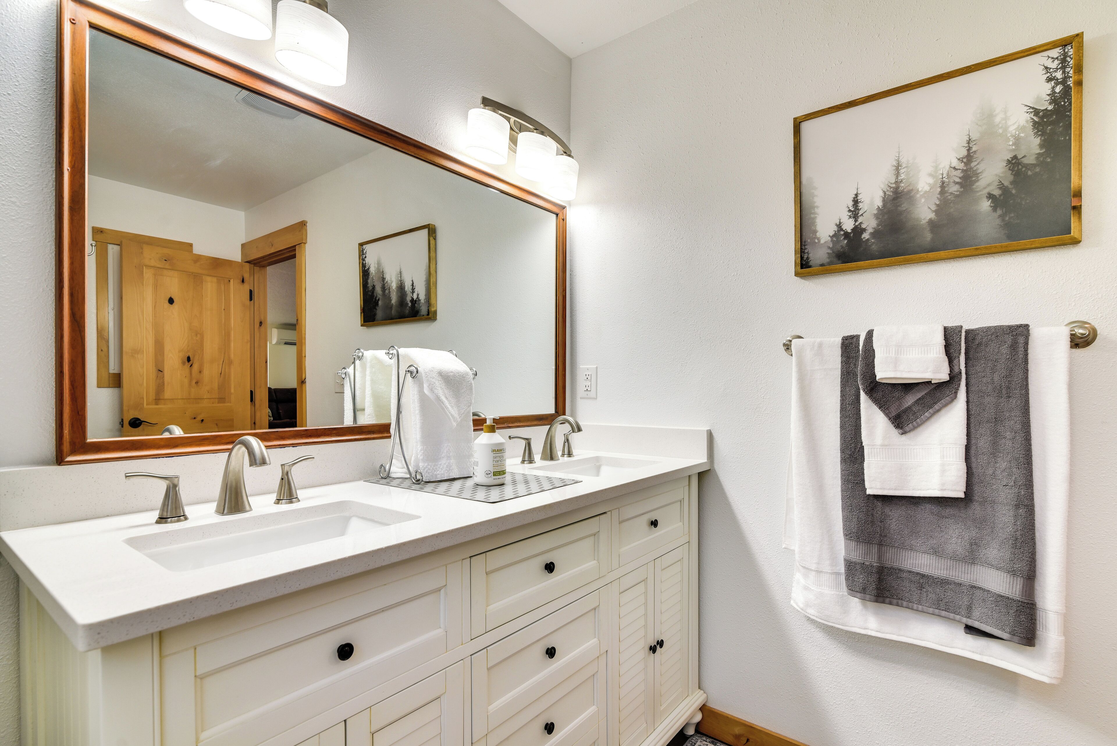 A bathroom with two sinks, a large mirror, and a towel rack with towels.