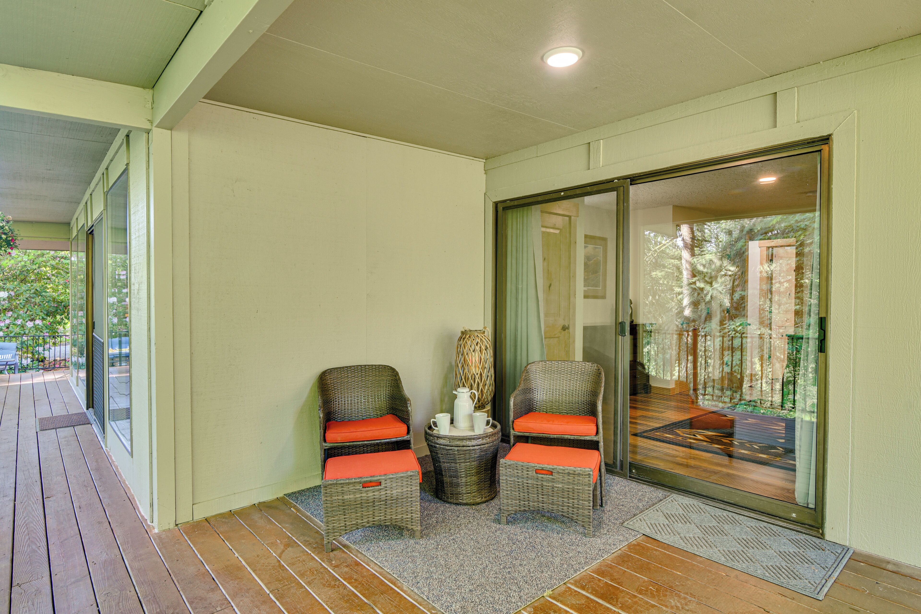 A covered outdoor seating area with wicker chairs and a table, a sliding glass door leading to a balcony, and a wooden deck.