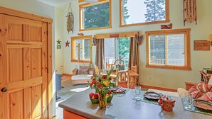 Interior acogedor de una cabaña con comedor, paredes de madera, ventanas amplias y vistas al bosque.