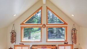 Una habitación con techos altos, vigas de madera triangulares y ventanas amplias que dan a un bosque.