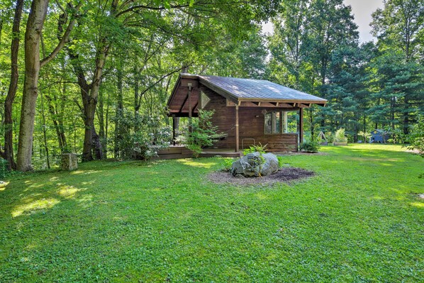 A wooden cabin with a sloped roof, surrounded by a well-maintained lawn and dense trees.