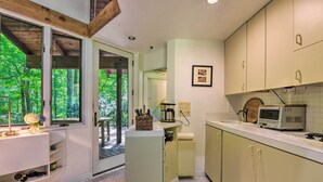 Eine moderne Küche mit weißen Schränken, einer eingebauten Mikrowelle und einem großen Fenster mit Blick auf den Wald.