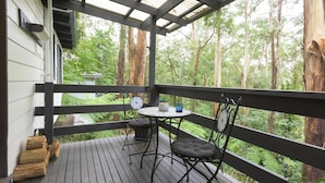 A wooden deck with a table and chairs, surrounded by tall trees.