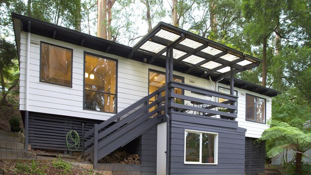 A modern two-story house with a wooden deck and a staircase leading to the upper floor.