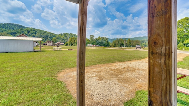 A view from a covered porch overlooking a grassy field with a building and mountains in the distance.