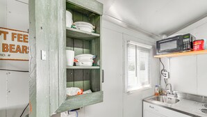 A kitchen with a wooden shelf holding dishes, a microwave, and a sink.