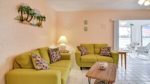 Ein Wohnzimmer mit zwei grünen Sofas, einem kleinen Tisch und einer Lampe. Es gibt Wandkunst und einen Blick auf den Balkon.