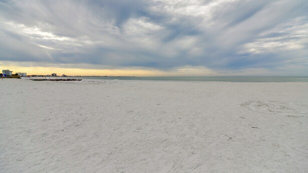 Ein weiter Sandstrand mit ruhiger See und bewölktem Himmel.