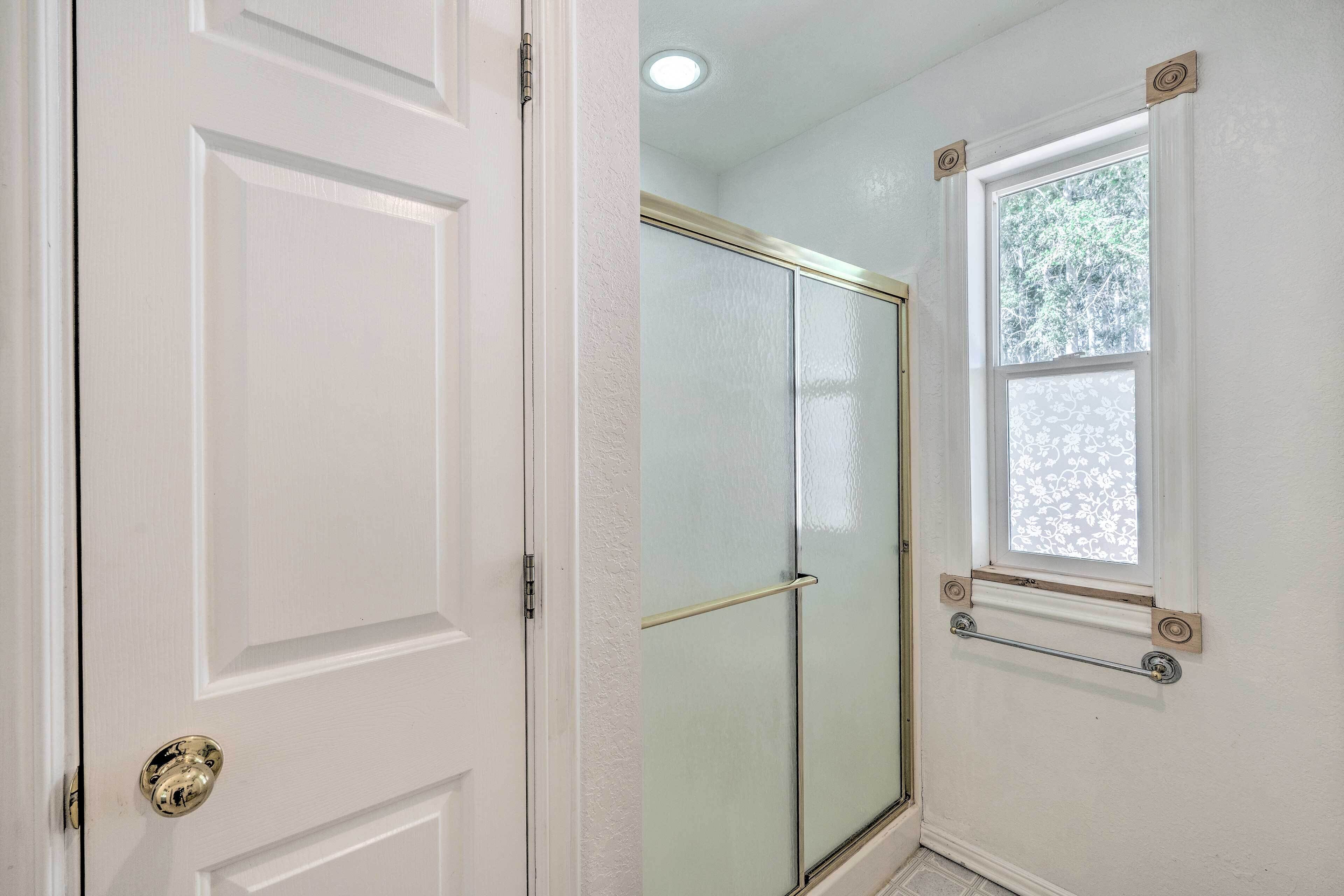 Un baño con puerta de vidrio para la ducha, un perchero y una ventana con vistas a árboles.