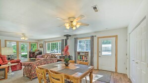 A spacious living room with a wooden dining table, chairs, and a ceiling fan. There is a fireplace, a sofa, and a bookshelf. - Caldwell Country Home on Quiet Acreage (Caldwell)