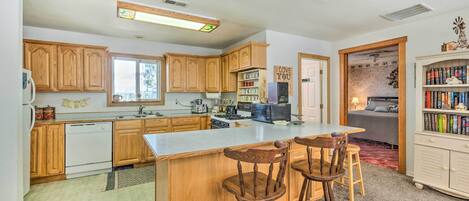 A kitchen with wooden cabinets, a central island with bar stools, a refrigerator, a stove, and a microwave.