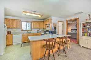 A kitchen with wooden cabinets, a central island with bar stools, a microwave, and a bookshelf.