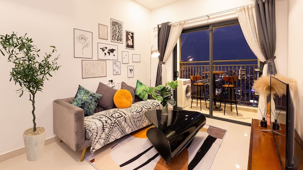 A modern living room with a sofa, a TV, and a balcony with a city view. - An Corner SOHO 3Bedrooms apt high floor nice view (Ho Chi Minh City)