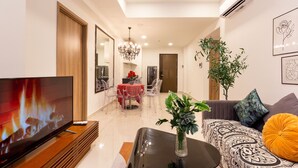 A modern living room with a flat-screen TV, a sofa, a coffee table, and a dining area with a red tablecloth. - An Corner SOHO 3Bedrooms apt high floor nice view (Ho Chi Minh City)