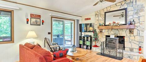 A cozy living room with a stone fireplace, a red sofa, a wooden coffee table, and a ceiling fan.