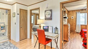 Une pièce comprenant un bureau en bois, une chaise, un lit avec une literie rouge, une fenêtre avec des rideaux et une porte donnant sur une autre pièce.