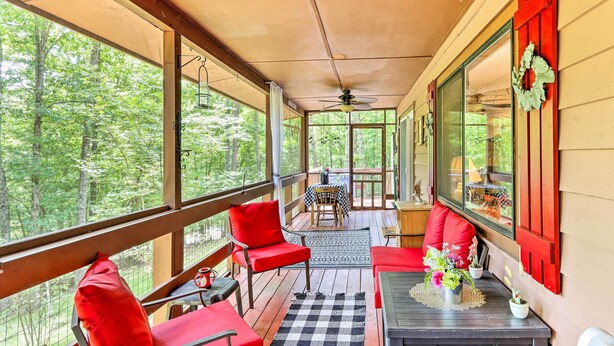 Une véranda avec des chaises rouges, une table décorée de fleurs et une vue sur les arbres.