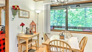 Un coin repas avec une table et des chaises en bois, un lustre et une fenêtre donnant sur les arbres.