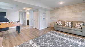 Ein Wohnzimmer mit einem Kicker, einem grauen Sofa mit gemusterten Kissen, einem Teppich mit Muster und einer Holzvertäfelung.