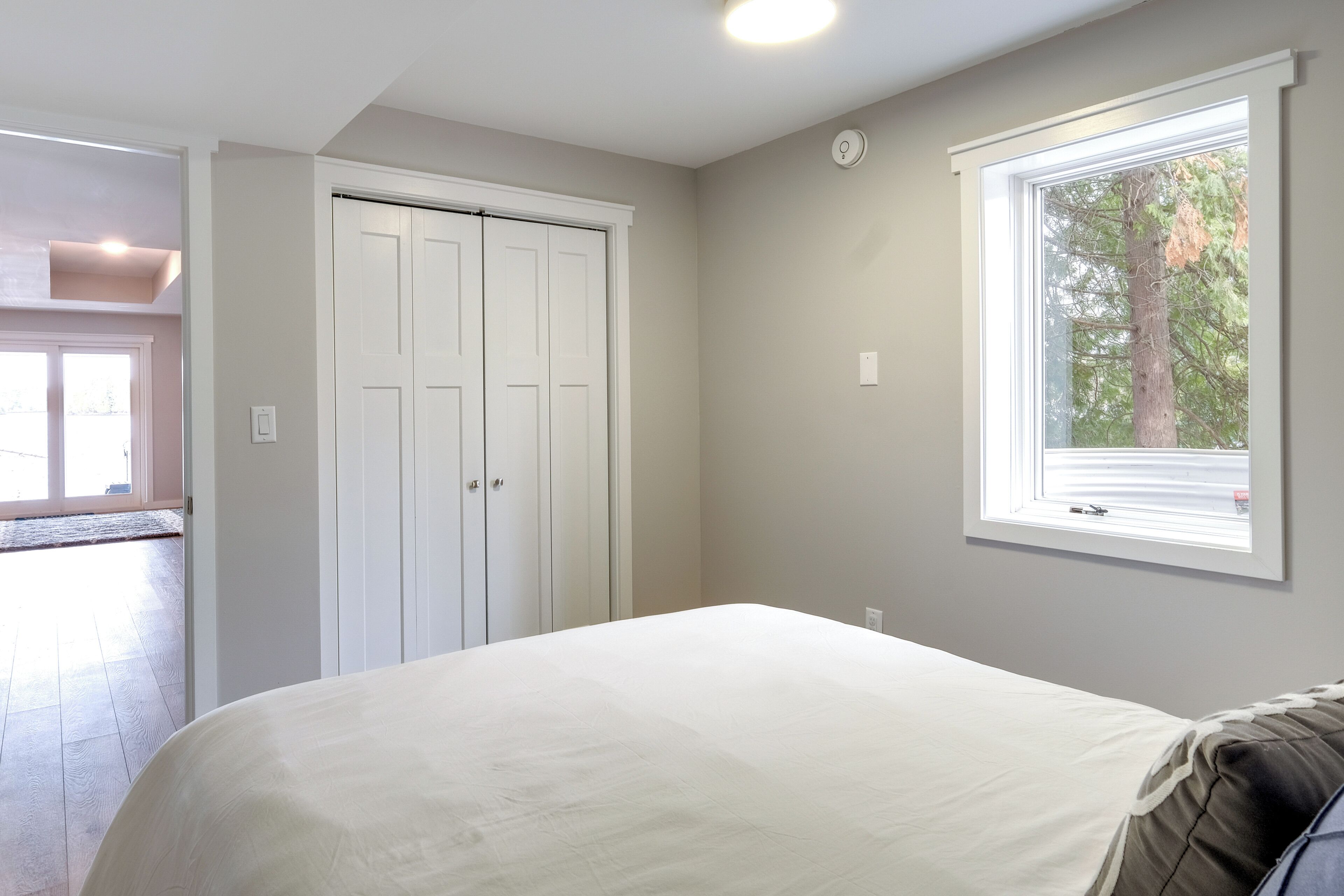 A bedroom with a bed, a window with a view of trees, and a white door.