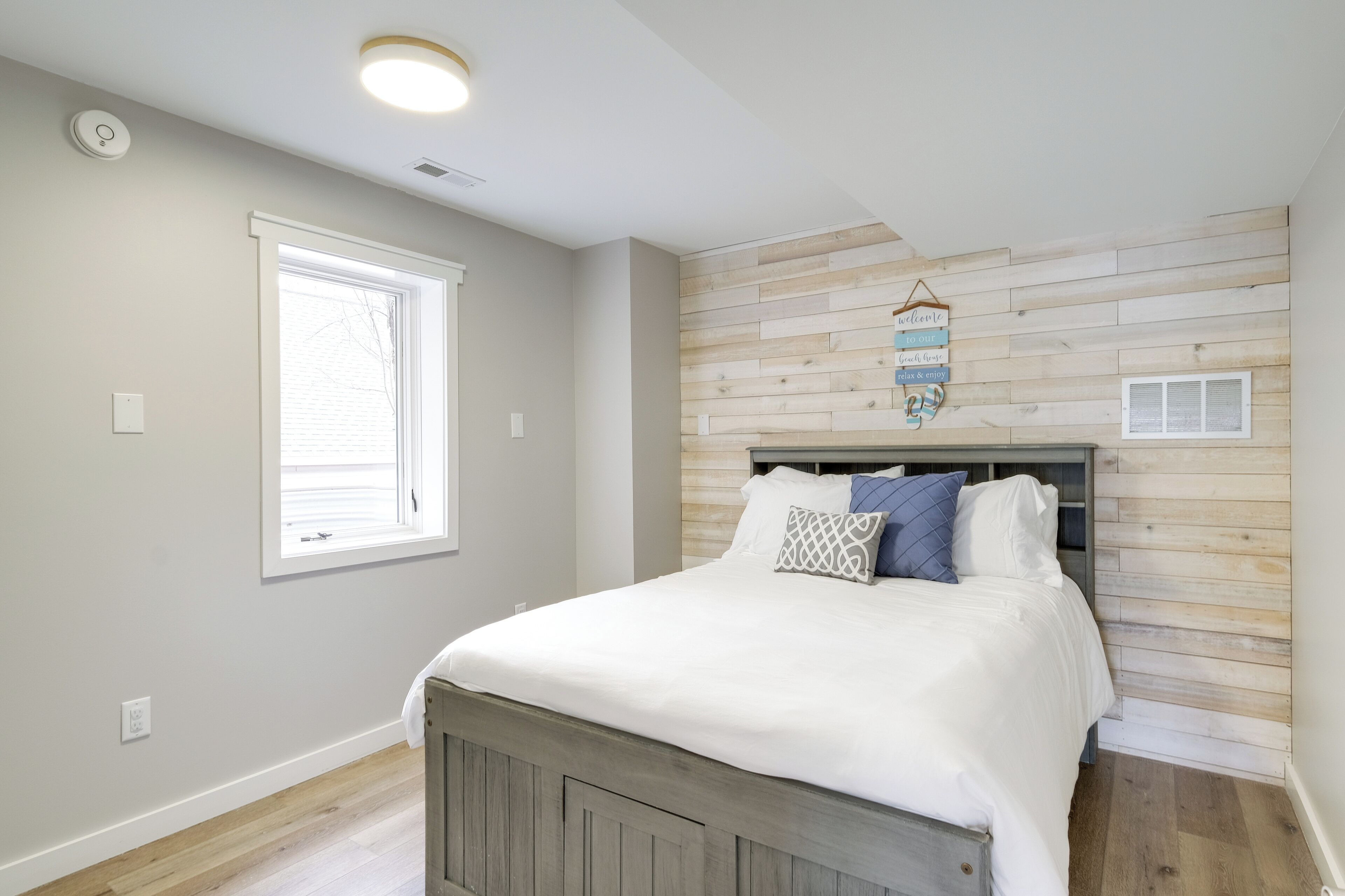 A bedroom with a bed, a window, a wall-mounted light, and a welcome sign.