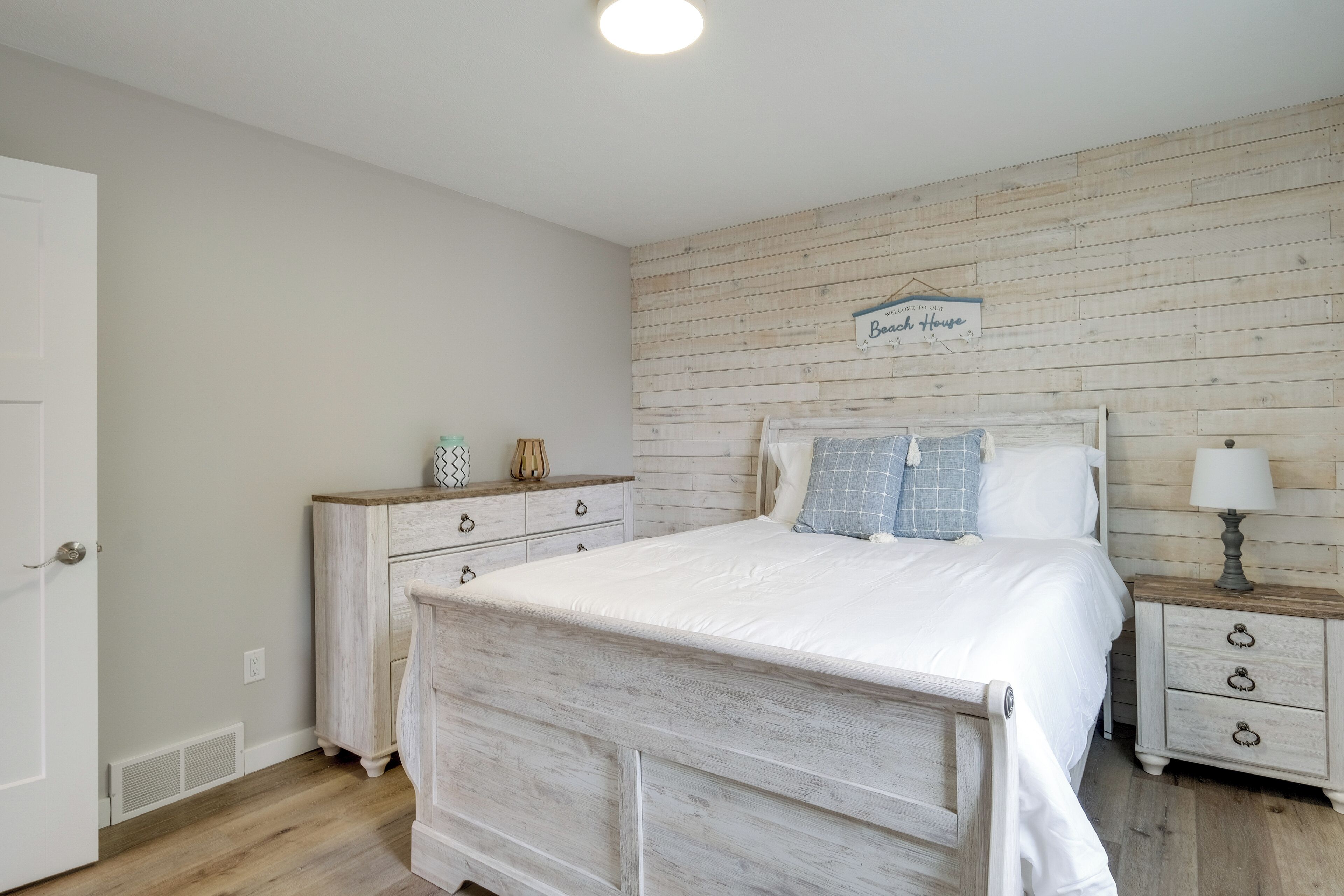 Un dormitorio con cabecera de madera, una mesita de noche con lámpara y un cartel en la pared.