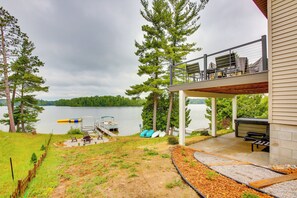 Een landhuis aan het meer met een overdekt terras, buitenmeubilair en een steiger met kajaks.