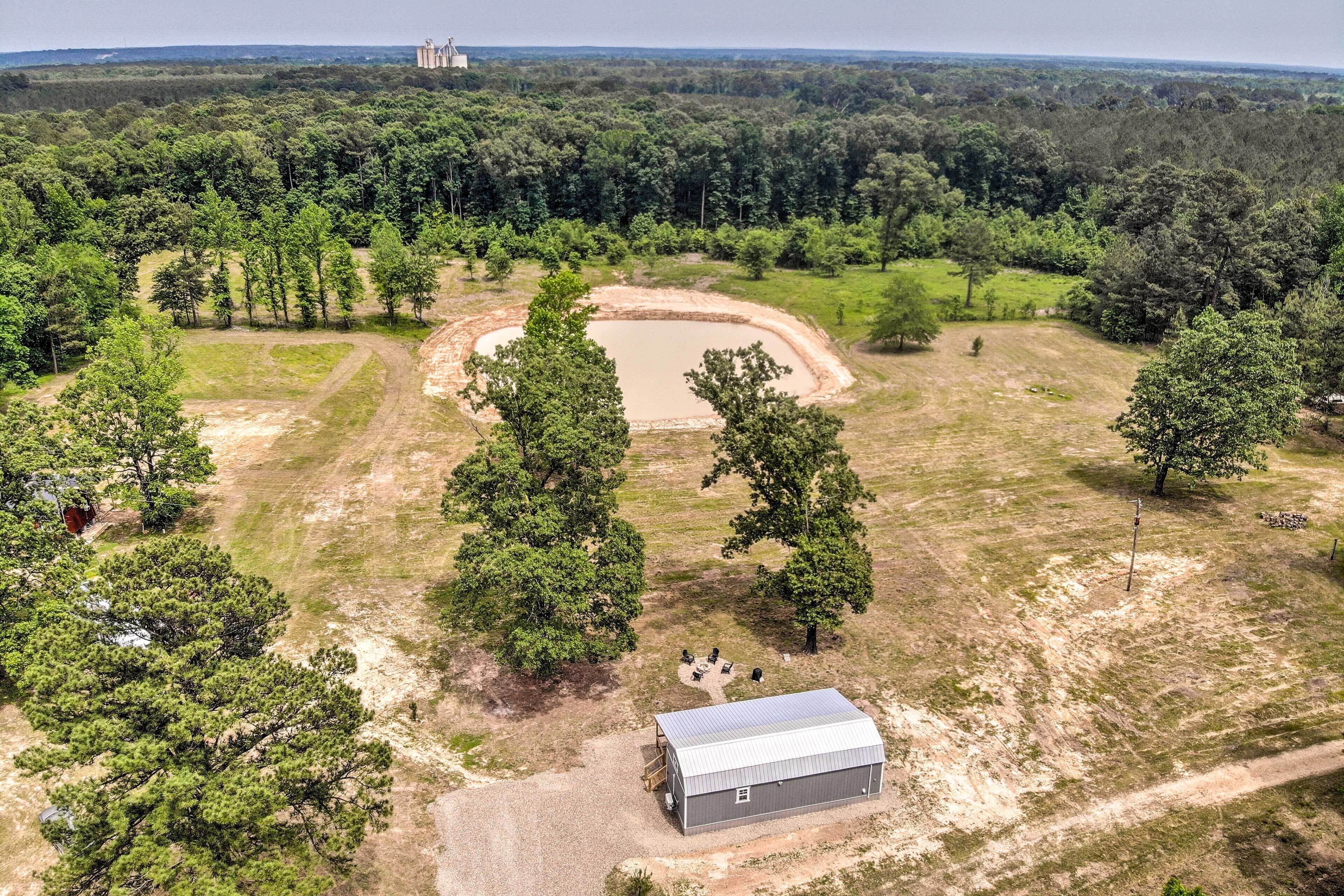 An aerial view of a rural property with a large pond, a barn, and surrounding forest.