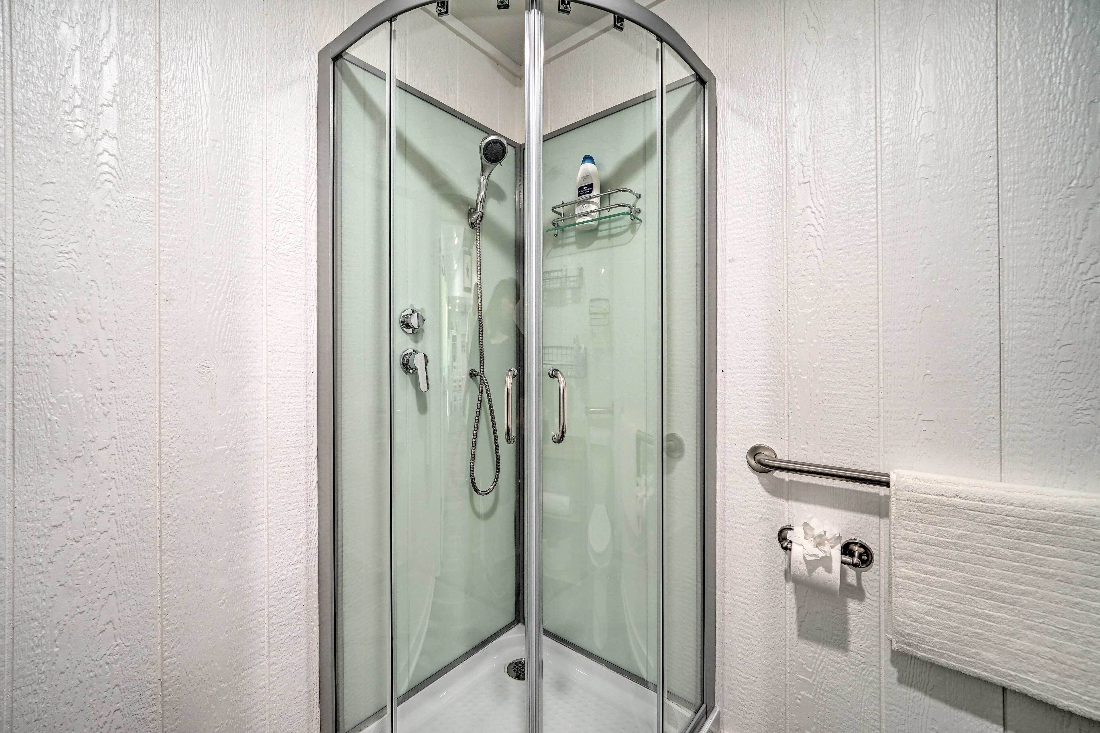 A glass-enclosed shower stall with a handheld showerhead, a glass shelf, and a towel rack.