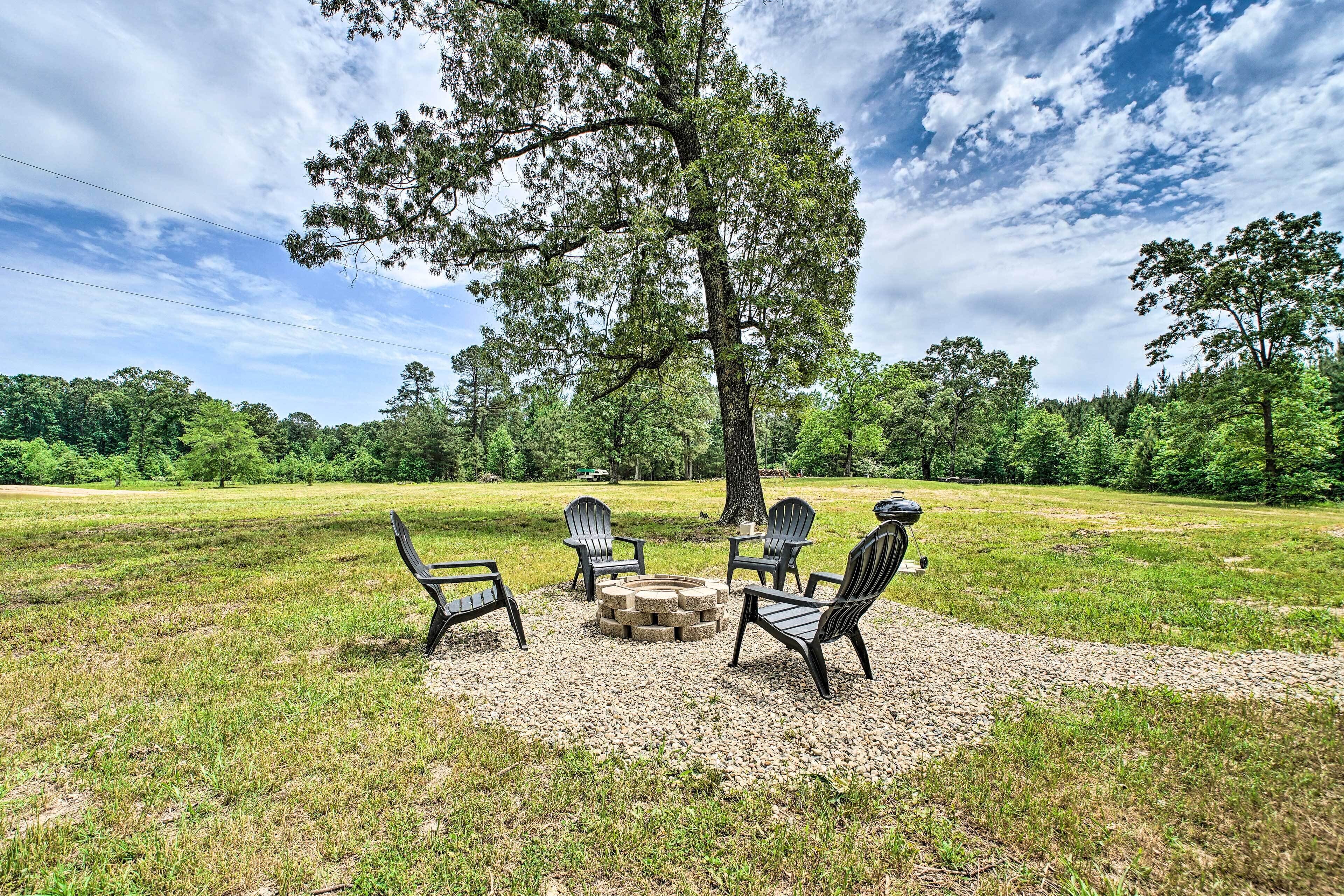 An outdoor seating area with a fire pit and chairs, surrounded by a grassy field and trees.