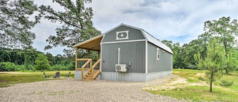 A rustic barn with a covered porch, gravel driveway, and outdoor seating area.