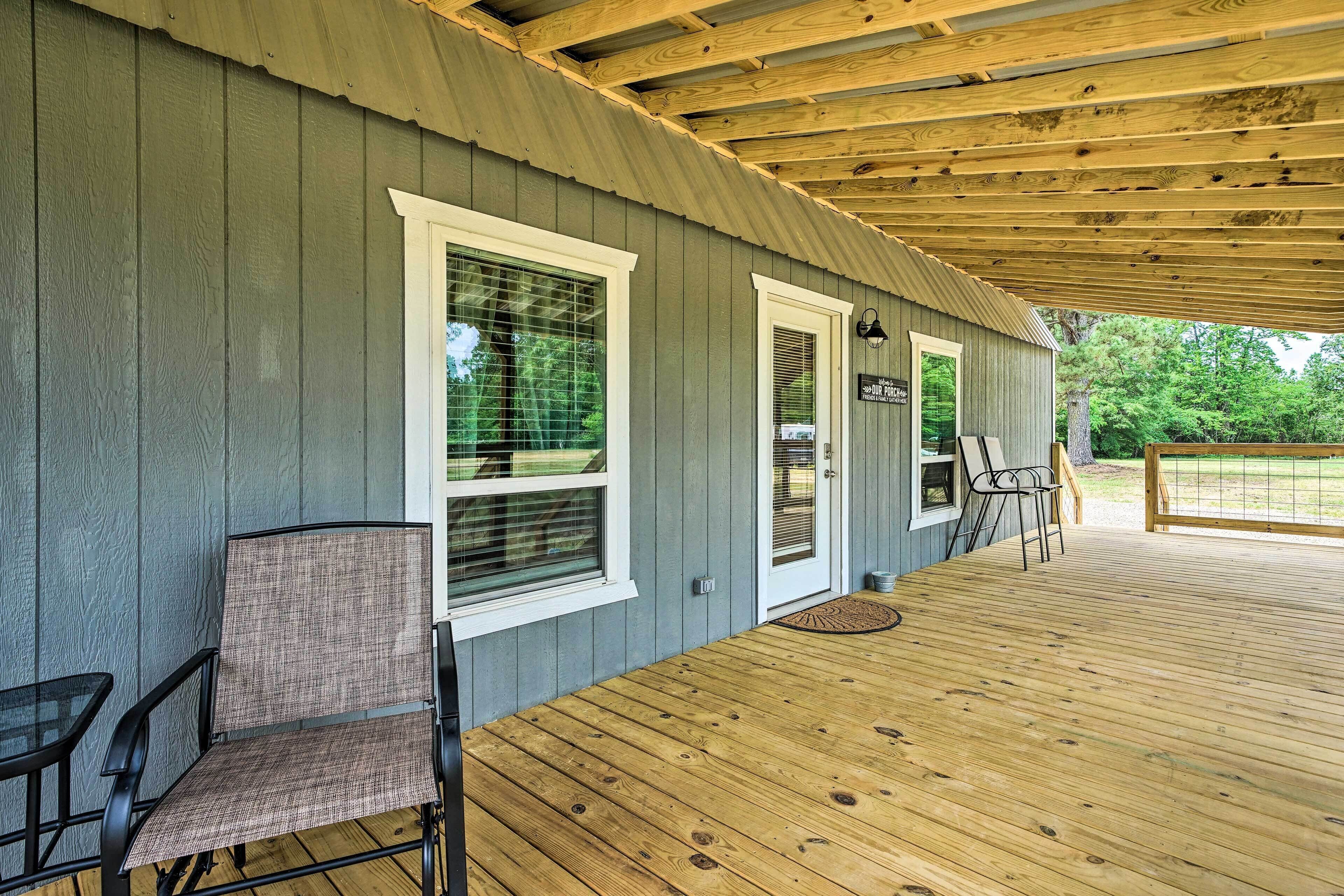 A covered porch with a wooden deck, two chairs, and a small table.