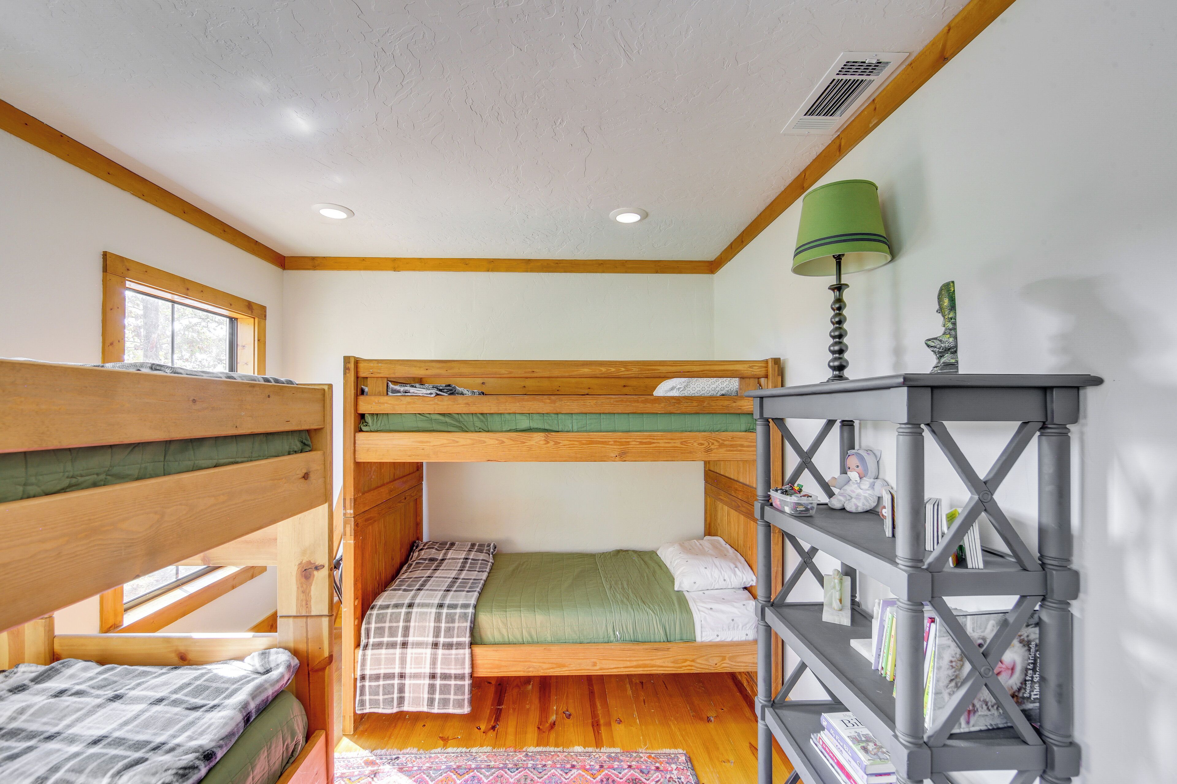 Habitación con literas, techo de madera, una ventana, una lámpara verde y una estantería.