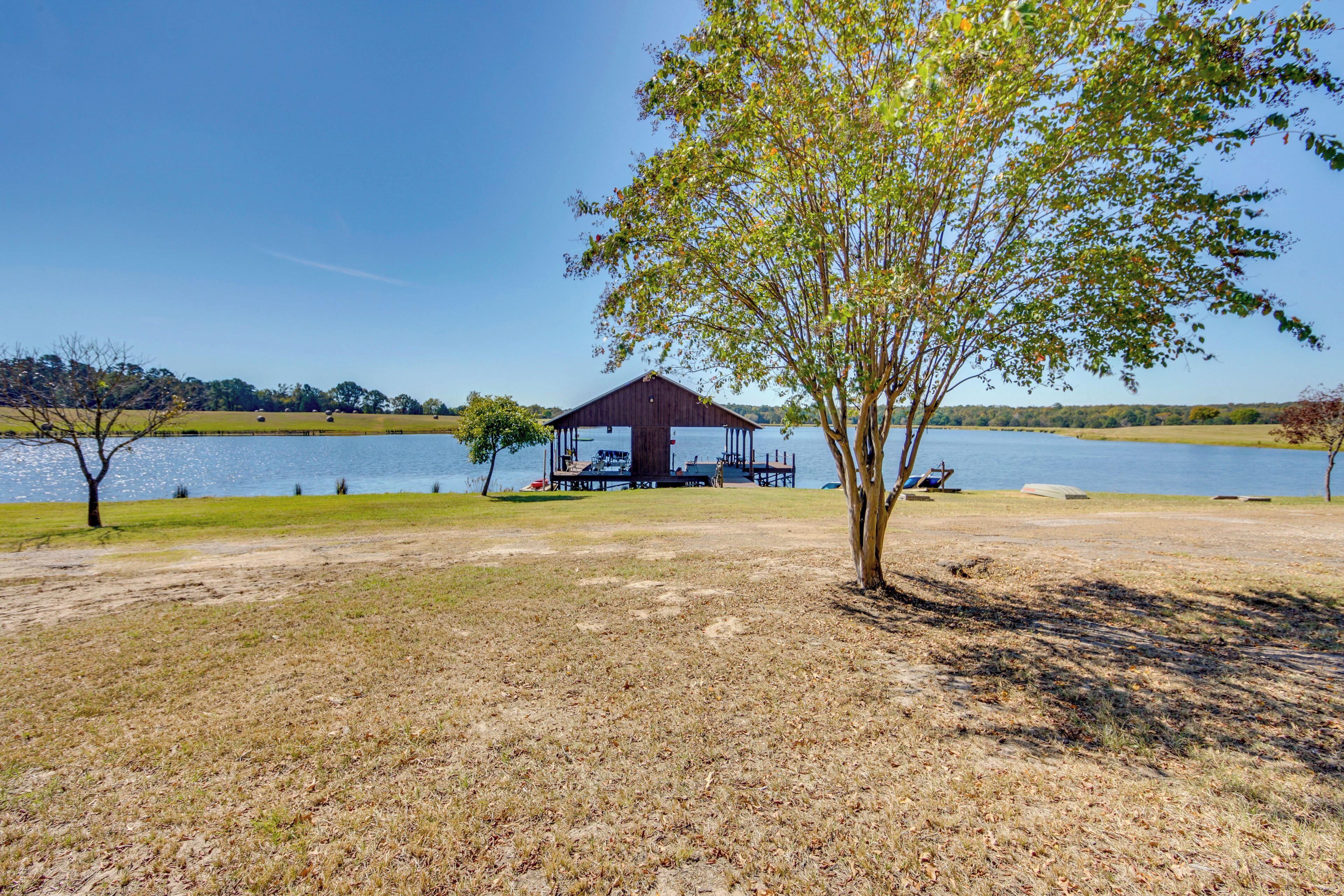 A lakeside pavilion with a covered seating area, surrounded by open grassy fields and a clear view of the lake.
