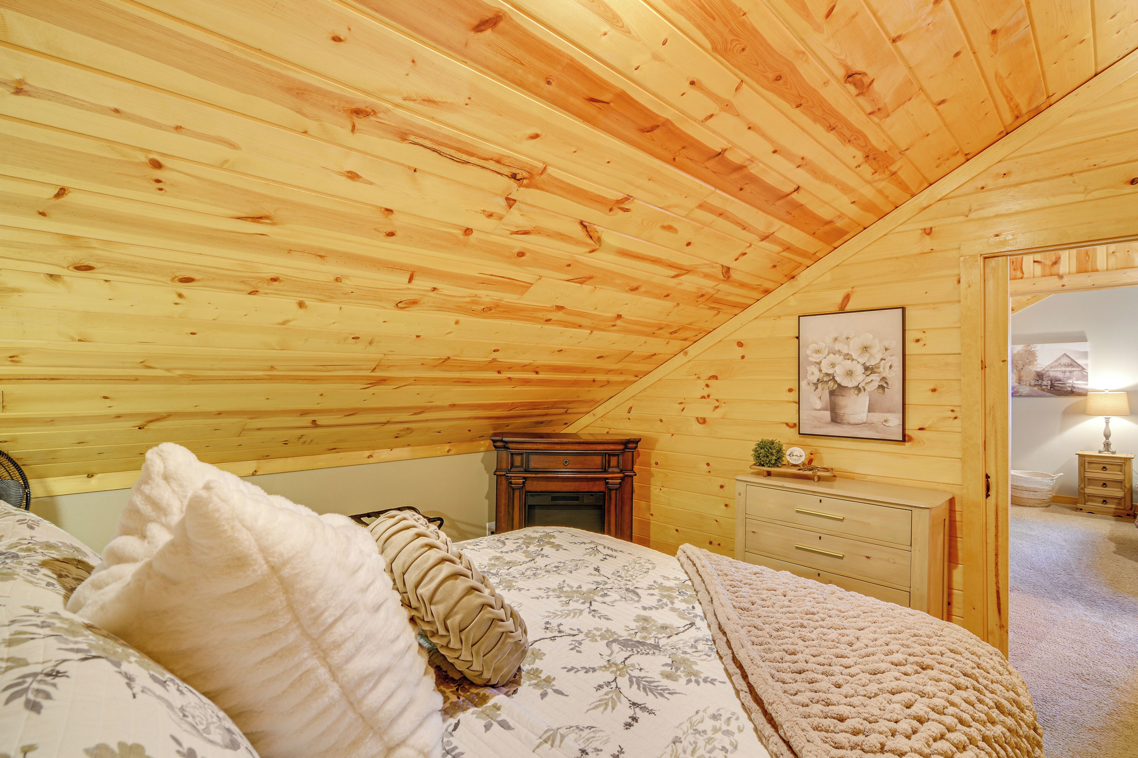 Ein gemütliches Schlafzimmer mit Holzbalken, einem Bett mit floralem Bettbezug, einem Schminktisch und einem gerahmten Bild an der Wand.