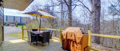 Een houten terras met buitenmeubilair, een barbecue en een overdekt gedeelte met een gele parasol.