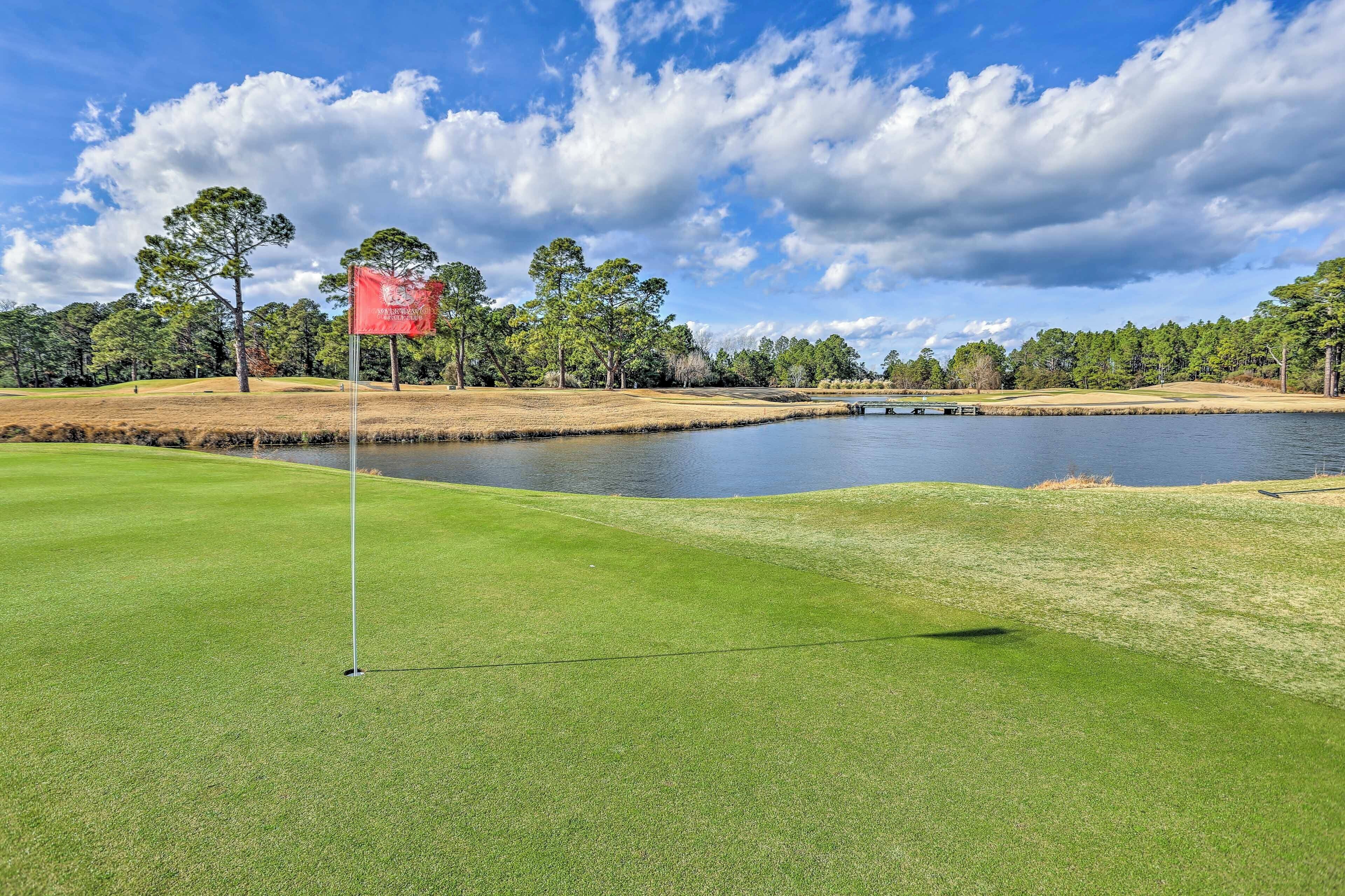 A golf course with a flagstick, water body, and trees.