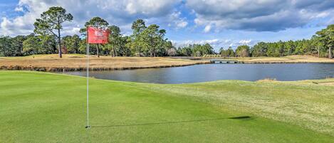 A golf course with a flagstick, water body, and trees.