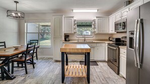 A kitchen with white cabinets, a wooden table, and a stainless steel refrigerator. - Granbury Cottage, Steps to Lake & Dock! (Granbury)